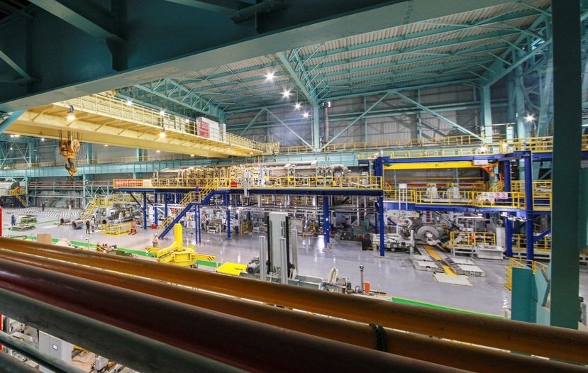 Operators at steel plant machine, inspecting large pipe production