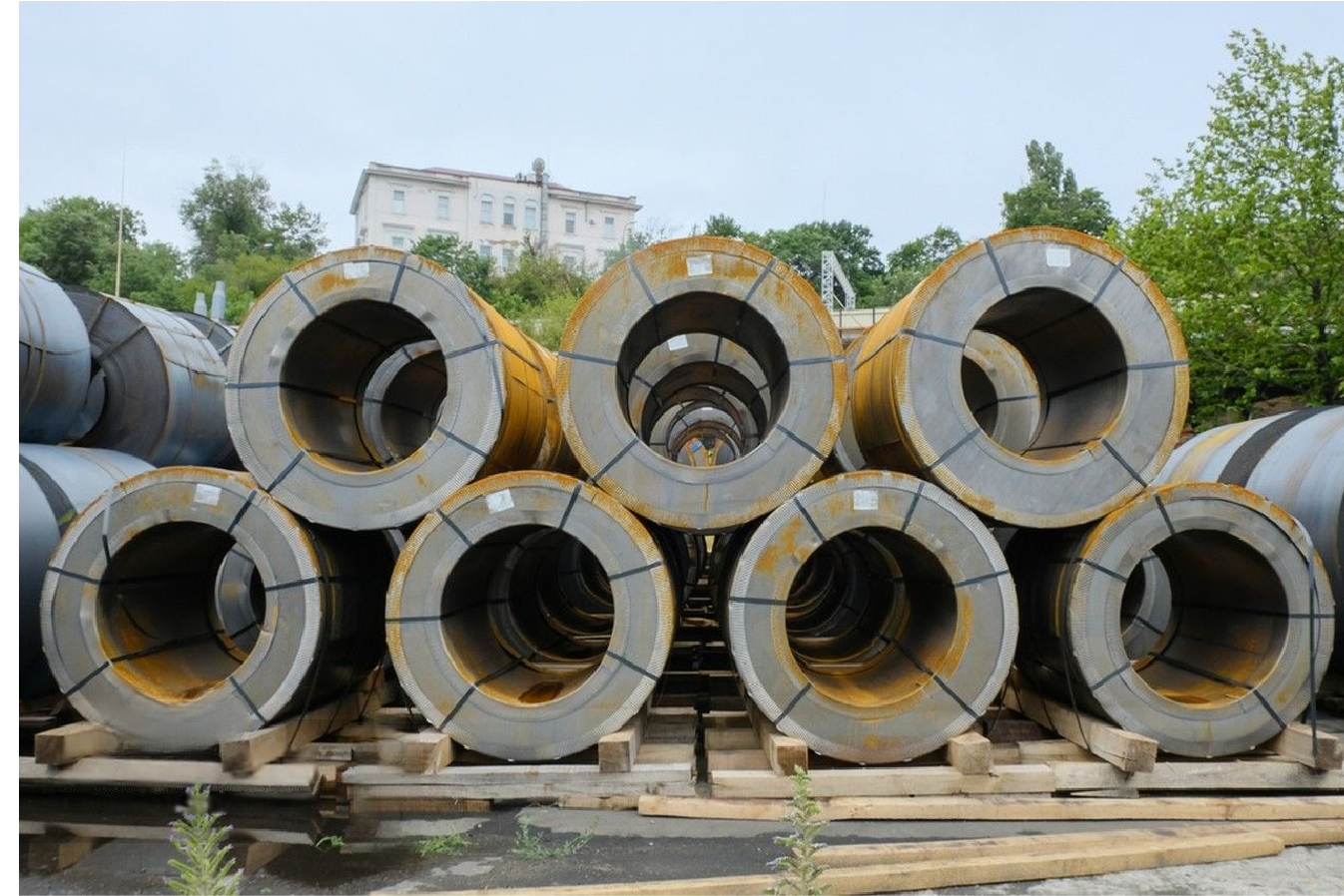 Exterior stacked steel coils with signs of oxidation, representing raw inventory awaiting surface treatment