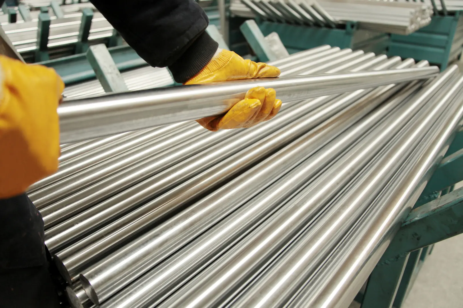Worker handling polished stainless steel tubes in manufacturing facility