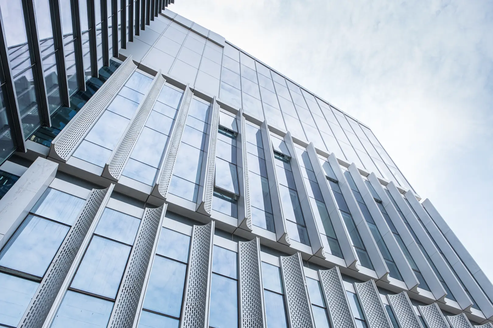 Contemporary building facade with sleek stainless steel panels and reflective glass windows under a bright sky