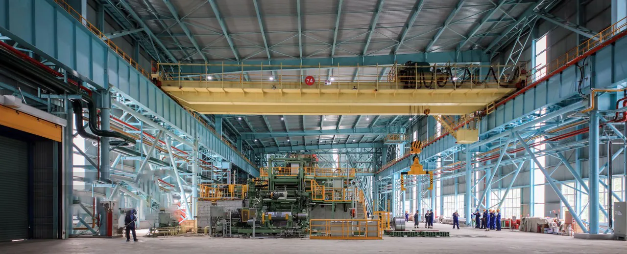 Interior view of a high-tech stainless steel manufacturing facility with machinery and workers.