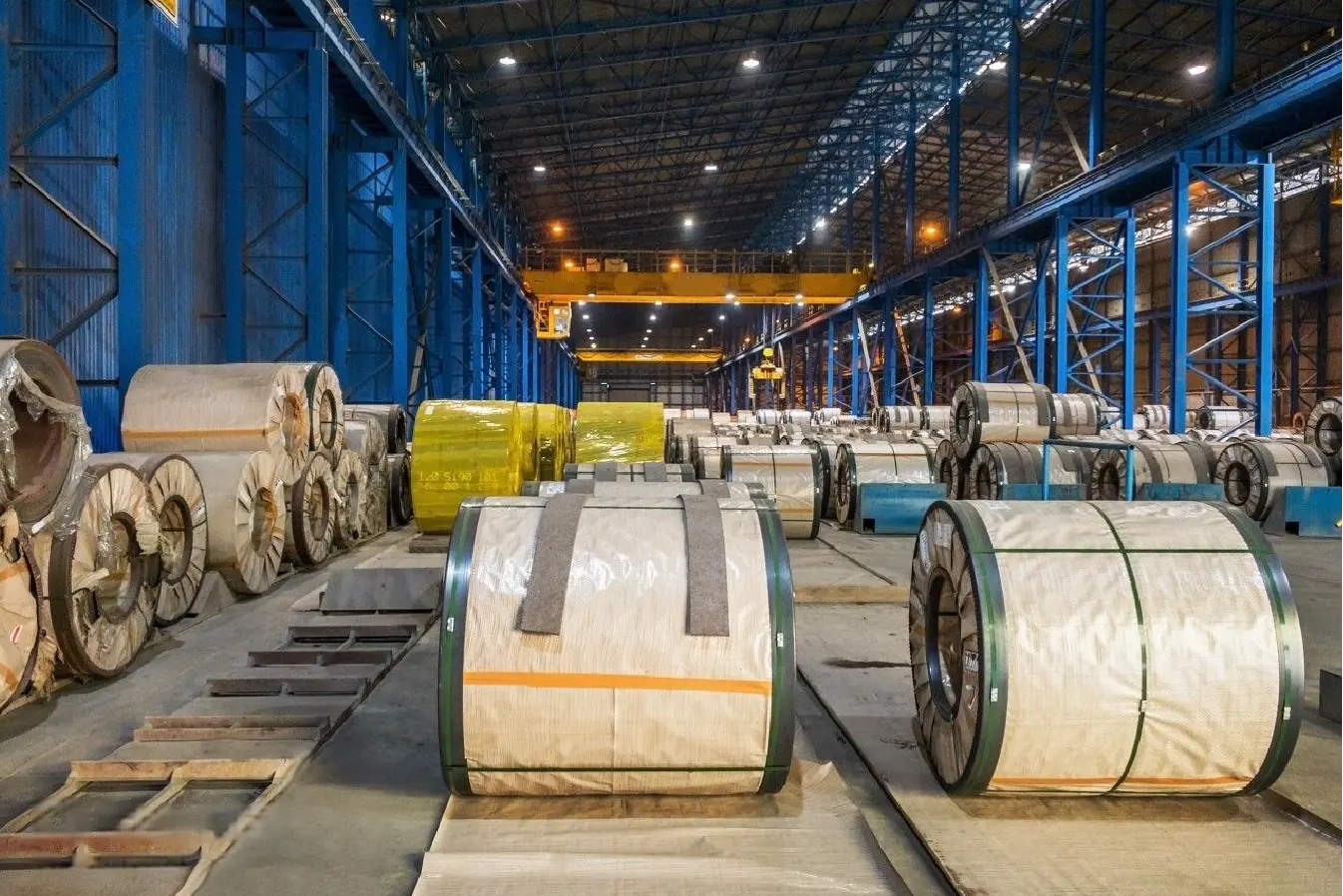 Interior view of a large warehouse with organized stacks of stainless steel coils ready for distribution.