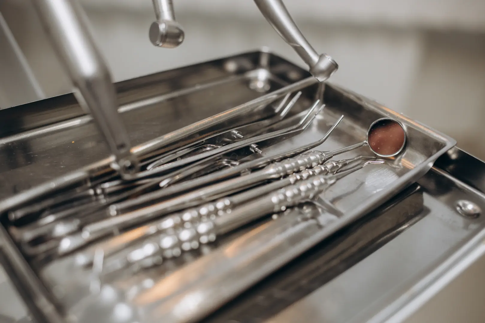 Close-up of stainless steel dental tools including mirror and probes on a metal tray