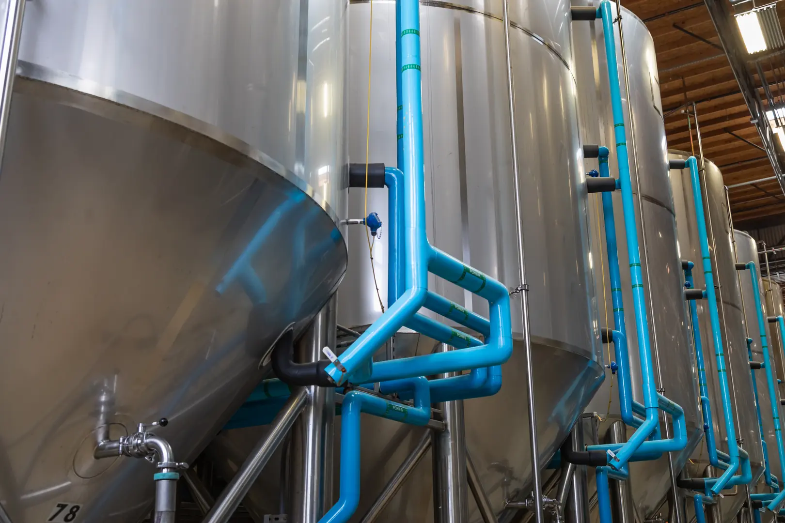 Large stainless steel tanks with blue pipes in an industrial setting