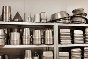 Shelves filled with various stainless steel kitchenware including pans, pots, and containers.