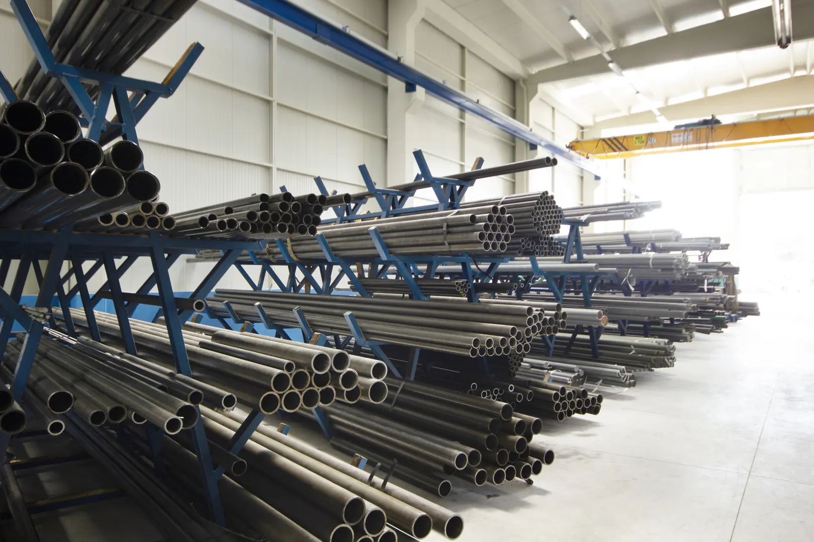 Warehouse with stacked stainless steel pipes on blue racks under industrial lighting